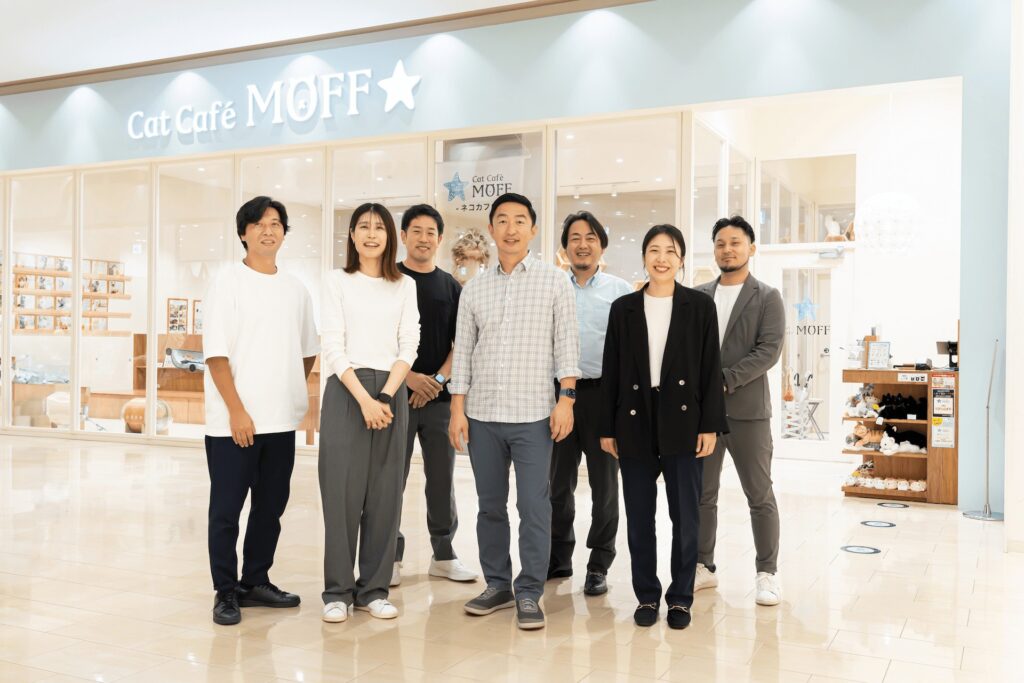 店舗前で複数の社員が笑顔で並ぶ写真：MOFF採用ページの集合イメージ